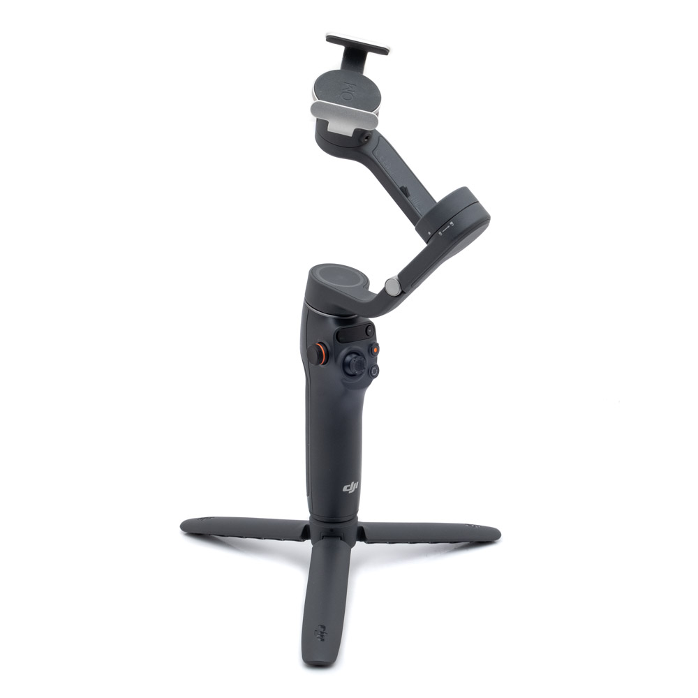 DJI Osmo Mobile 6-1 Käytetty DJI Osmo Mobile 6 (Kunto K5, Takuu 6kk) musta käsikäyttöinen älypuhelimen gimbal-stabilisaattori, jossa on jalusta, seisoo pystyssä valkoisella taustalla.