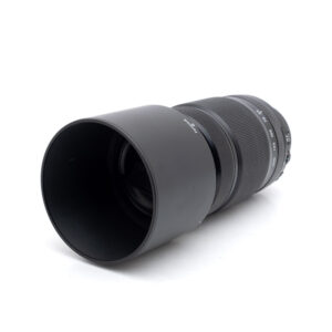 Fujinon XF 55-200mm f/3.5-4.8 R LM OIS (sis.ALV24%) - Käytetty teleobjektiivi mustana, suurella vastavalosuojalla, valkealla taustalla, jotta sen etulasi ja kuvioidut tarkennusrenkaat tulevat esiin.