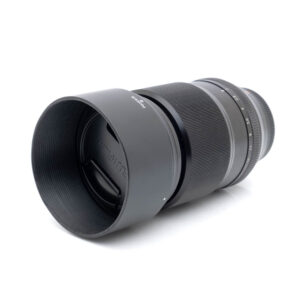 Fujinon 90mm f2-1 Fujinon XF 90mm f/2 R LM WR - Käytetty objektiivi mustana, kuvassa vastavalosuoja kiinnitettynä valkoisella taustalla, kuvakulmassa, jossa etuelementti ja osa tarkennusrenkaasta on näkyvissä.
