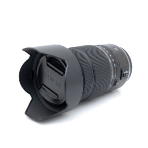 Fujinon GF 45-100mm f4-1 Käytetty Fujinon GF 45-100mm f/4 R LM OIS WR -objektiivi (sis. ALV 25,5%), jossa on vastavalosuoja ja suojus, mustat kuvioidut zoom- ja tarkennusrenkaat sekä näkyvät sivukytkimet valkoisella pohjalla.