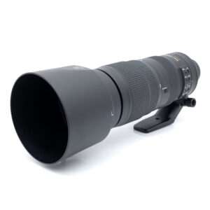 Nikkor 200-500mm f5.6-1 Nikon AF-S Nikkor 200-500mm f/5.6E ED VR - Käytetty on suuri musta teleobjektiivi, jossa on kuvioitu kahva, vastavalosuoja ja jalustakiinnitys, kuvassa valkoisella pohjalla.