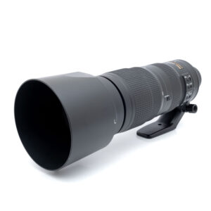 Nikkor 200-500mm f5.6ED-1 Suuri musta Nikon AF-S Nikkor 200-500mm f/5.6E ED VR -teleobjektiivi (käytetty), jossa on vastavalosuoja, jalustapanta ja ohjauskytkimet tynnyrissä, kuvakulmasta katsottuna.