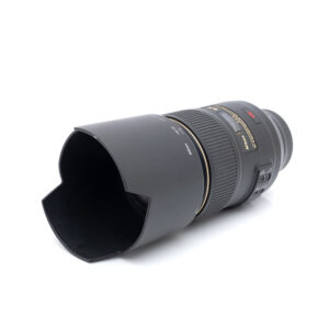 Nikkor AF-S 105mm f2.8-1 Nikon AF-S Micro-Nikkor 105mm f/2.8G VR ED - Käytetty -objektiivi, johon on kiinnitetty terälehden muotoinen huppu, valkoista taustaa vasten.