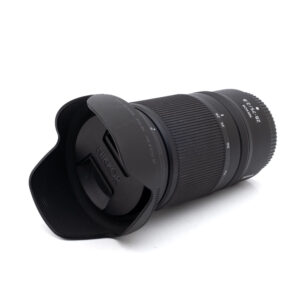 Musta Nikon Nikkor Z 28-75mm f/2.8 -objektiivi (Kunto K5, Takuu 6kk, ALV24%) - Käytetty, jossa on vastavalosuoja ja suojus kiinnitettynä, kuvioidut pitorenkaat ja näkyvät polttovälin ja aukon merkinnät valkoisella pinnalla.