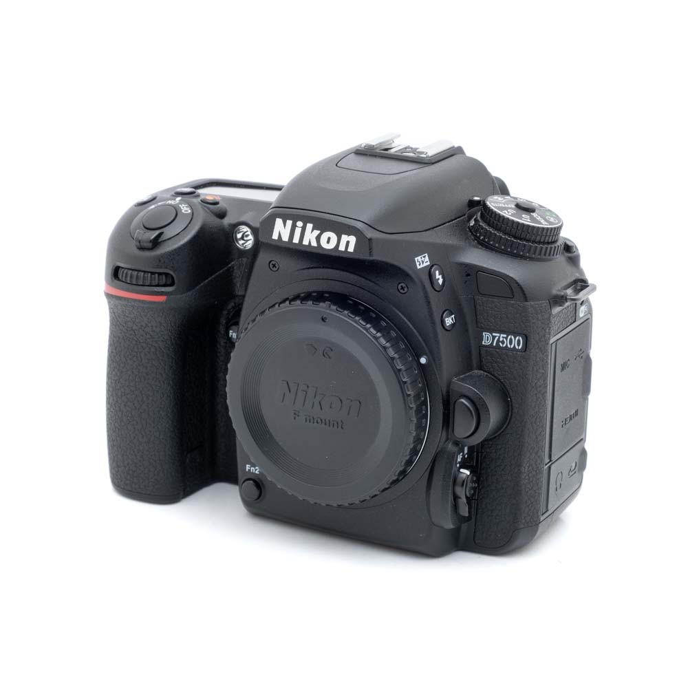 Nikon D7500-1 Nikon D7500 (SC 28000) - Käytetty DSLR-kameran runko ja objektiivin suojus etupuolelta valkoisella taustalla.