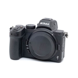 Nikon Z5-1 Nikon Z5 (K5, SC 2500) - Käytetty peilitön kamerarunko on kuvassa mustana, hieman oikealle päin, objektiivin kiinnityssuojus kiinni ja ilman objektiivia.