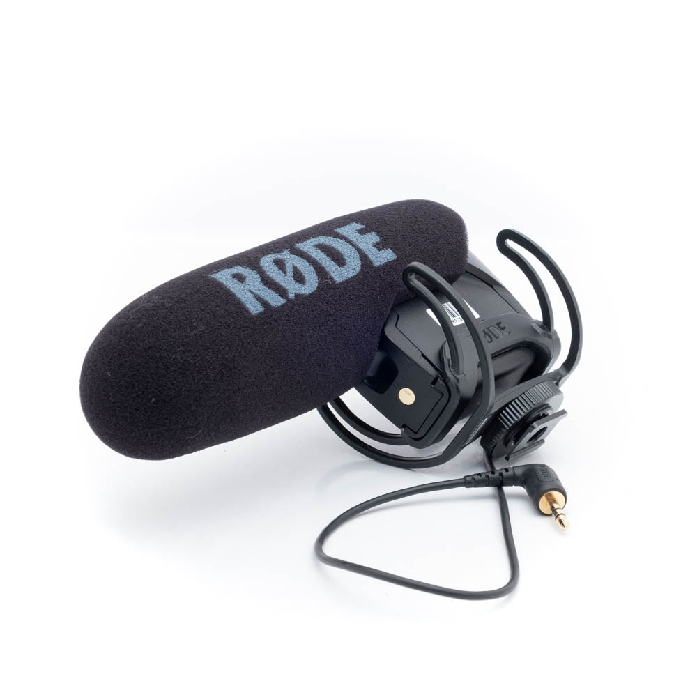 Rode Videomic Pro-1 Käytetty Rode VideoMic Pro (Kunto K5), jossa on musta vaahtomuovinen tuulisuoja ja iskukiinnike, 3,5 mm:n ääniliitin kiinnitettynä, näytetään valkoisella pohjalla.