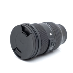 Sigma 24-70mm f2.8 DG DN Sony-1 Sigma Art 24-70mm f/2.8 DG DN Sony - Käytetty objektiivi mustana, objektiivin suojus kiinnitettynä, kyljellään valkoista taustaa vasten.