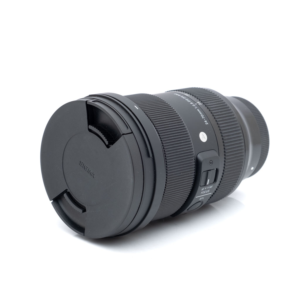 Sigma 24-70mm f2.8 DG DN Sony-1 Sigma Art 24-70mm f/2.8 DG DN Sony - Käytetty objektiivi mustana, objektiivin suojus kiinnitettynä, kyljellään valkoista taustaa vasten.