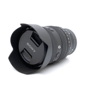 Sony 20-70mm f4 G-1 Sony FE 20-70mm f/4 G - Käytetty kameran objektiivi, johon on kiinnitetty vastavalosuoja, valkoisella taustalla. Objektiivin suojuksessa näkyy Sonyn logo.