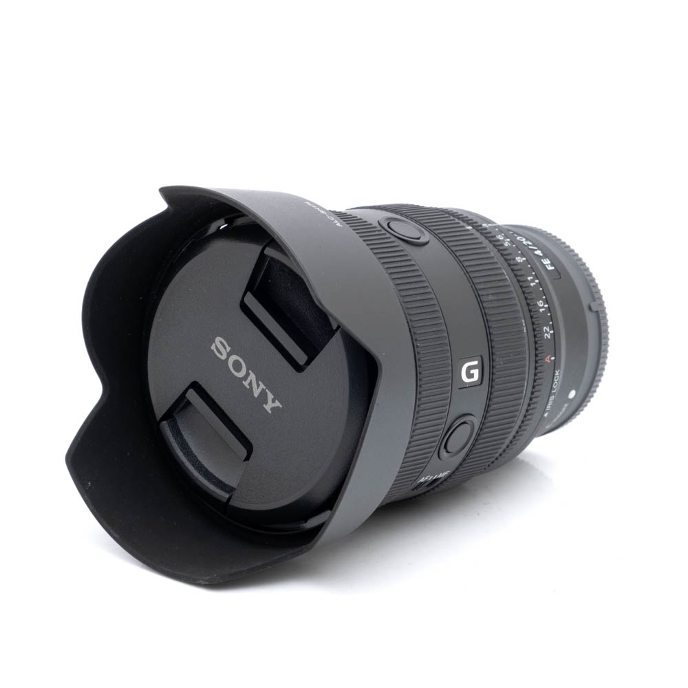 Sony 20-70mm f4 G-1 Sony FE 20-70mm f/4 G - Käytetty kameran objektiivi, johon on kiinnitetty vastavalosuoja, valkoisella taustalla. Objektiivin suojuksessa näkyy Sonyn logo.