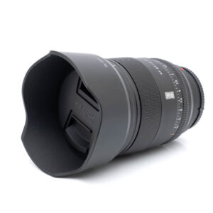 Viltrox AF PRO 27mm f/1.2 Fuji (Kunto K5) - Käytetty kameran objektiivi, johon on kiinnitetty vastavalosuoja ja suojus, vinossa valkoisella taustalla.