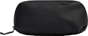 800q-01_128331 Mustassa Peak Design Tech Pouch Small -laukussa on sileä rakenne, minimaalinen tuotemerkintä ja pieni tunniste vetoketjun vieressä vaaleaa taustaa vasten.