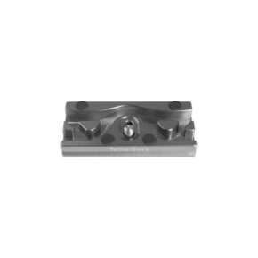 Tether Tools TetherBlock Arca Graphite on metallinen kameran lisävaruste, jossa on keskiruuvi ja urat kaapeleiden kiinnittämiseen valokuvauksen aikana. Se on esillä valkoisella pohjalla.