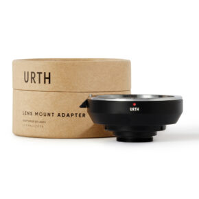 1677857025_302 Musta Urth Canon EF - C Mount objektiiviadapteri istuu sen lieriömäisen ruskean pahvipakkauksen edessä, jossa lukee "Urth Lens Mount Adapter", molemmat näkyvät valkoista taustaa vasten.