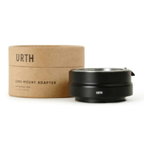 1678090116_758 Musta Urth Pentax K - Canon RF objektiiviadapteri istuu sen lieriömäisen pahvilaatikon vieressä, jossa lukee URTH Lens Mount Adapteri valkoisella taustalla.