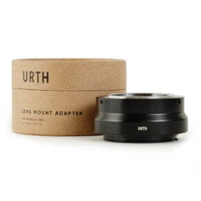 1678090155_836 Musta Urth M42 - Canon RF objektiiviadapteri lepää sen lieriömäisen pahvipakkauksen vieressä, jossa lukee "URTH" ja "Lens Mount Adapter" mustalla tekstillä valkoisella pohjalla.
