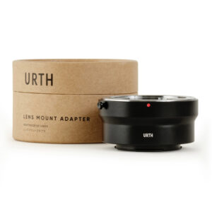 1678090225_663 Musta Urth Contax/Yashica (C/Y) - Fujifilm X objektiiviadapteri näkyy sen pyöreän, ruskean pahvisen pakkauksen vieressä, jossa lukee Urth Lens Mount Adapter.