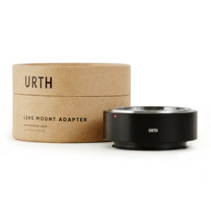 1678090384_606 Musta Urth Konica AR - Leica L objektiiviadapteri näkyy sen lieriömäisen ruskean URTH-laatikon vieressä. Adapterissa on metallinen reunus ja pieni punainen piste.