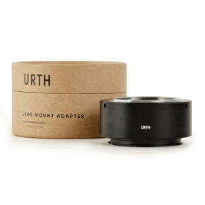 Musta Urth M42 - Leica L objektiiviadapteri istuu sen lieriömäisen ruskean pahvisen pakkauksen vieressä, jossa on merkintä URTH Lens Mount Adapter valkoisella pohjalla.
