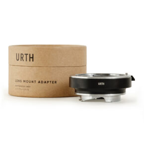 1678090687_192 Lieriömäinen pahvilaatikko, jossa lukee "Urth Leica R - Leica M objektiiviadapteri", on metallisen ja mustan kameran objektiivin kiinnityssovittimen vieressä, molemmat valkoisella pohjalla.