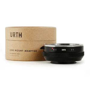 1678090705_801 Musta Urth Sony A (Minolta AF) - Micro Four Thirds (M4/3) objektiiviadapteri istuu ruskean sylinterimäisen laatikon vieressä, jossa on merkintä URTH Lens Mount Adapter, valkoisella taustalla.
