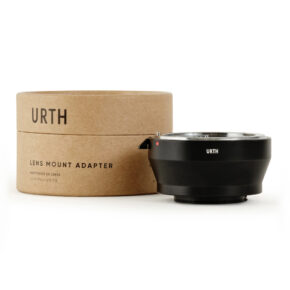 1678090898_700 Musta Urth Nikon F - Nikon 1 objektiiviadapteri istuu sen lieriömäisen ruskean pahvipakkauksen vieressä, jossa lukee "URTH LENS MOUNT ADAPTER" valkoisella taustalla.