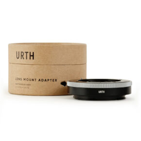 1678091033_345 Urth Contax G - Nikon Z objektiiviadapteri näkyy sen ruskean lieriömäisen laatikon vieressä, jossa on merkintä URTH LENS MOUNT ADAPTER. Musta adapteri, jossa on hopeinen rengas, on sijoitettu pakkauksen eteen.