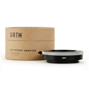 1678091033_345 Urth Contax G - Nikon Z objektiiviadapteri näkyy sen ruskean lieriömäisen laatikon vieressä, jossa on merkintä URTH LENS MOUNT ADAPTER. Musta adapteri, jossa on hopeinen rengas, on sijoitettu pakkauksen eteen.