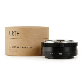1678091113_426 Musta Urth Canon FD - Nikon Z objektiiviadapteri näytetään sen lieriömäisen ruskean pahvipakkauksen vieressä, jossa lukee "URTH LENS MOUNT ADAPTER" valkoisella pohjalla.