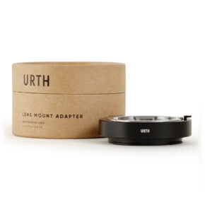 1678091133_633 Urth Leica M - Nikon Z objektiiviadapteri istuu sen lieriömäisen, ruskean pakkauksen vieressä, jossa on tuotteen nimi. Mustassa sovittimessa on Urthin logo.
