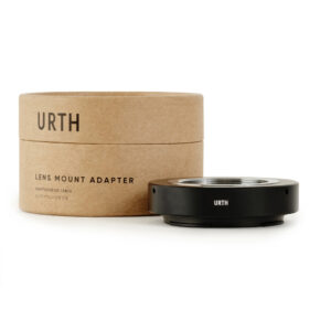1678091150_523 Pyöreä pahvilaatikko, jossa lukee "Urth M39 - Nikon Z objektiiviadapteri", on mustan metallisen objektiiviasennussovittimen vieressä, molemmat valkoisella pohjalla.