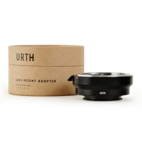 1678091233_441 Urth Nikon F - Samsung NX objektiiviadapteri on sijoitettu sen sylinterimäisen ruskean pahvipakkauksen viereen, jossa lukee mustalla "URTH Lens Mount Adapter". Adapteri on musta ja siinä on hopeinen sisärengas.