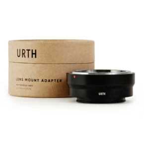 1678091286_895 Musta Urth Konica AR - Sony E objektiiviadapteri näkyy sen pyöreän, ruskean pahvisen pakkauksen edessä, jossa lukee "URTH Lens Mount Adapter". Adapterissa on metallinen reunus ja pieni punainen merkkipiste.