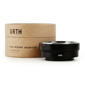1678091286_895 Musta Urth Konica AR - Sony E objektiiviadapteri näkyy sen pyöreän, ruskean pahvisen pakkauksen edessä, jossa lukee "URTH Lens Mount Adapter". Adapterissa on metallinen reunus ja pieni punainen merkkipiste.