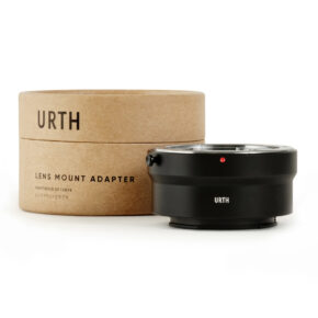1678091951_954 Musta Urth Contax/Yashica (C/Y) - Sony E objektiiviadapteri istuu sen pyöreän, ruskean pahvilaatikon vieressä, jossa on merkintä URTH Lens Mount Adapter, ja molemmat on sijoitettu tavalliselle valkoiselle taustalle.