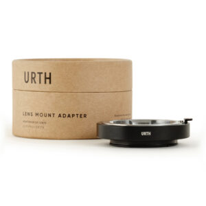 1678092480_558 A brown cylindrical box with the words "Urth Leica M - Sony E lens adapter" is next to a black metal lens mount adapter with "URTH" printed on it, both placed on a white background.