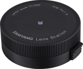 800q-01_118763 Samyang Lens Station - Fuji X is a black, round device with textured edges marked OPEN, CLOSE and FOR FUJI X. It updates the firmware of the lens and adjusts the settings of Fuji X lenses.