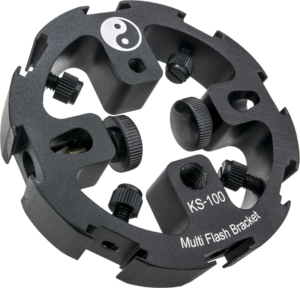800q-01_122743 Musta pyöreä metallilaite, jossa on merkintä Kupo KS-100 Bagua Multiflash Bracket, jossa on useita säätönuppeja ja yin-yang-symboli yläosassa.