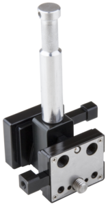 800q-01_122868 Kupo KS-275 Dual V-Lock Adapter on metallista ja mustasta muovista valmistettu komponentti, jossa on sylinterinmuotoinen kahva, neliönmuotoinen pohja, etulevy, jossa on ruuvinreiät, ja kaksi pyöreää aukkoa.