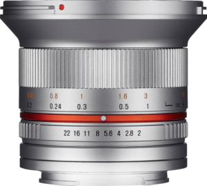 800q-06_SAMYANG-12MM-F2 Samyang 12mm f/2.0 NCS CS Fuji X (hopea) -objektiivin lähikuvassa näkyy punainen korostusrengas ja kaiverretut etäisyys- ja aukkomerkinnät mustalla ja oranssilla värillä valkoista taustaa vasten.
