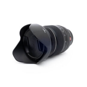 Fuji 16-55mm WR-3 Fujinon XF 16-55mm f/2.8 R LM WR - Käytetty -objektiivi näkyy valkoisella taustalla, kun sen terälehden muotoinen vastavalosuoja on kiinnitetty, etuelementti ja vastavalosuoja on käännetty katsojaan päin.
