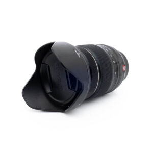 Fuji 16-55mm WR-3 Fujinon XF 16-55mm f/2.8 R LM WR - Käytetty -objektiivi näkyy valkoisella taustalla, kun sen terälehden muotoinen vastavalosuoja on kiinnitetty, etuelementti ja vastavalosuoja on käännetty katsojaan päin.