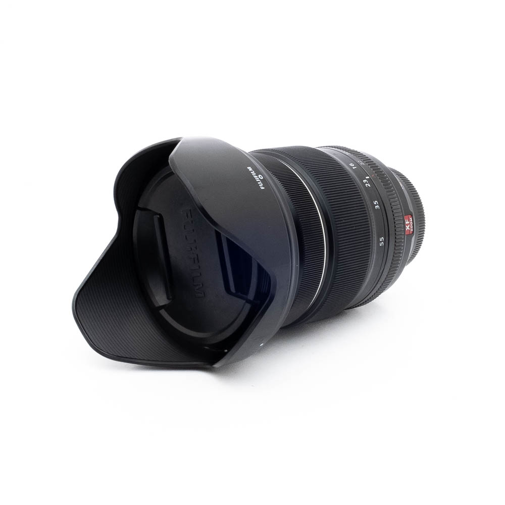 Fuji 16-55mm WR-3 Fujinon XF 16-55mm f/2.8 R LM WR - Käytetty -objektiivi näkyy valkoisella taustalla, kun sen terälehden muotoinen vastavalosuoja on kiinnitetty, etuelementti ja vastavalosuoja on käännetty katsojaan päin.