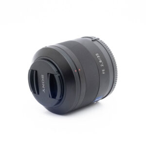 Sony 35mm f28 ZA-3 Musta Sony FE 35mm f/2.8 Sonnar T* ZA -objektiivi (käytetty), jossa on objektiivin suojus, asetetaan pienessä kulmassa valkoiselle pinnalle.