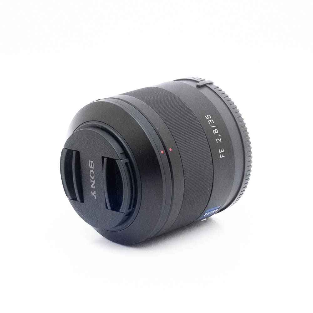 Sony 35mm f28 ZA-3 Musta Sony FE 35mm f/2.8 Sonnar T* ZA -objektiivi (käytetty), jossa on objektiivin suojus, asetetaan pienessä kulmassa valkoiselle pinnalle.