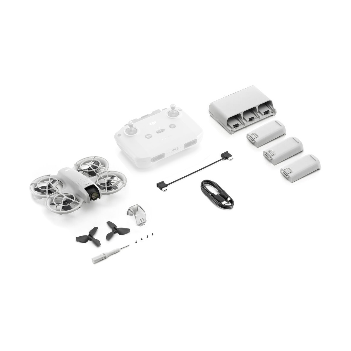 Valkoisella pinnalla esitelty DJI Neo Fly More Combo -dronipakkaus sisältää lennokin, kauko-ohjaimen, kolme akkua, latauskeskittimen, potkurit, ruuvimeisselin, ruuvit, USB-kaapelin ja pieniä sovittimia.