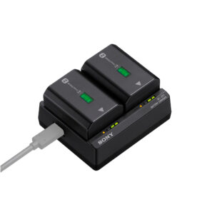 1.-BC-ZD1-Battery-Charger Sony BC-ZD1 Laturi -mustassa akkulaturissa on kaksi kameran akkua, joissa molemmissa on vihreät valot, ja se saa virtansa valkoisesta USB-kaapelista.