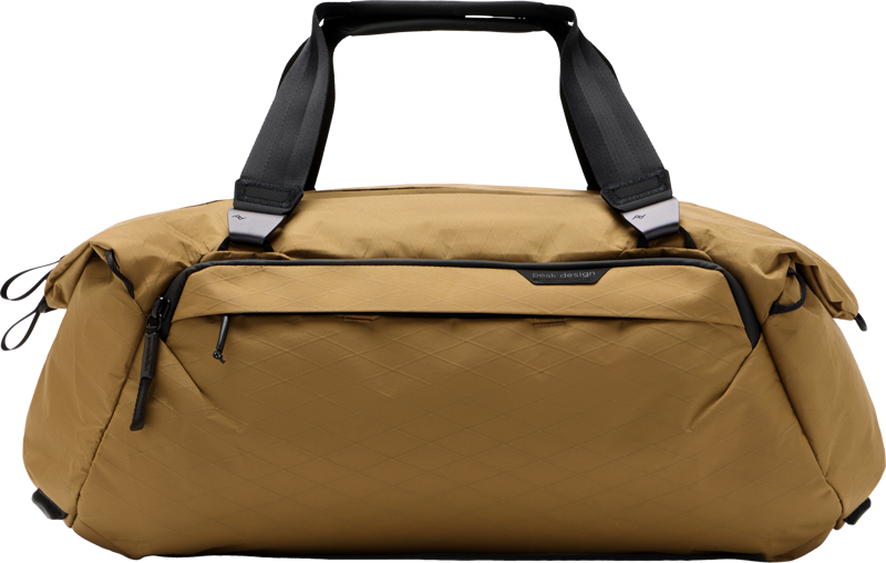 Peak Design Travel Duffel 35L - Coyote -laukussa on mustat kahvat ja vetoketjut, timanttikuvioinen rakenne ja vetoketjullinen etutasku, joka näkyy vaalealla pohjalla.