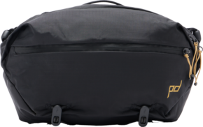 The Peak Design Outdoor Sling 7L - Black features a front zip, gold logo lettering on the bottom right corner, tan zipper pulls on the right side and two adjustable straps at the bottom.